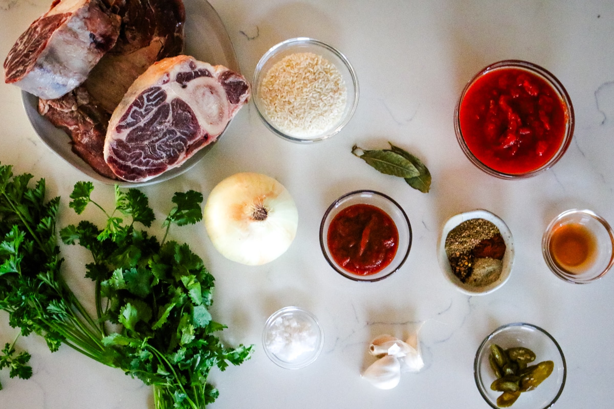Ingredients for kharcho soup arranged on a table, including beef, rice, tomatoes, onions, garlic, herbs, and spices.