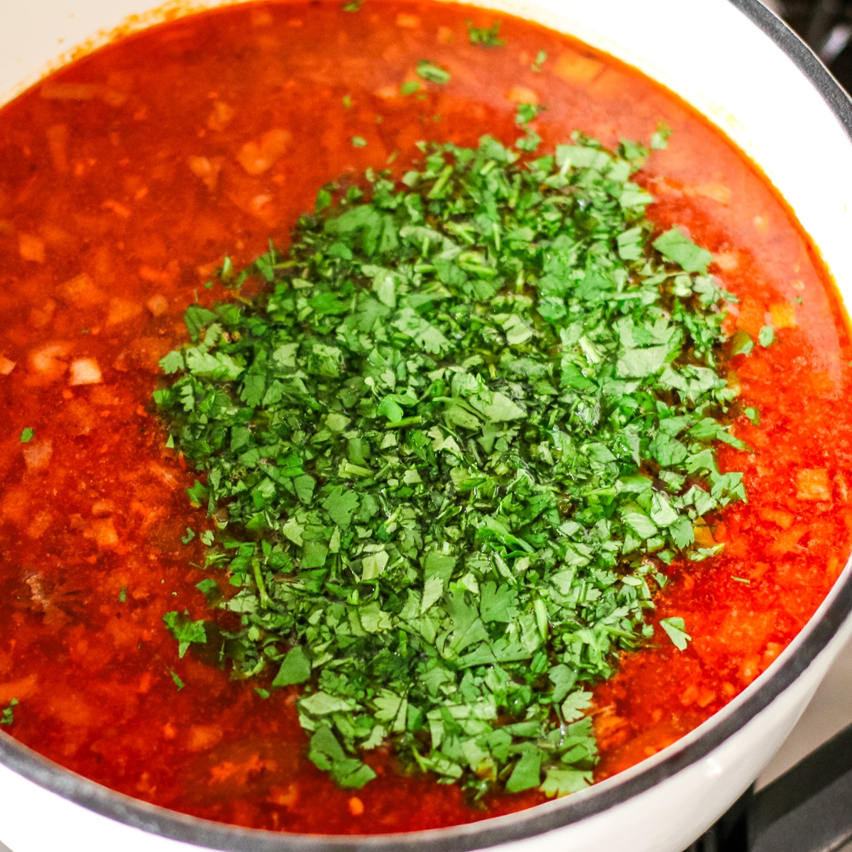 kharcho soup with fresh herbs in a white pot.