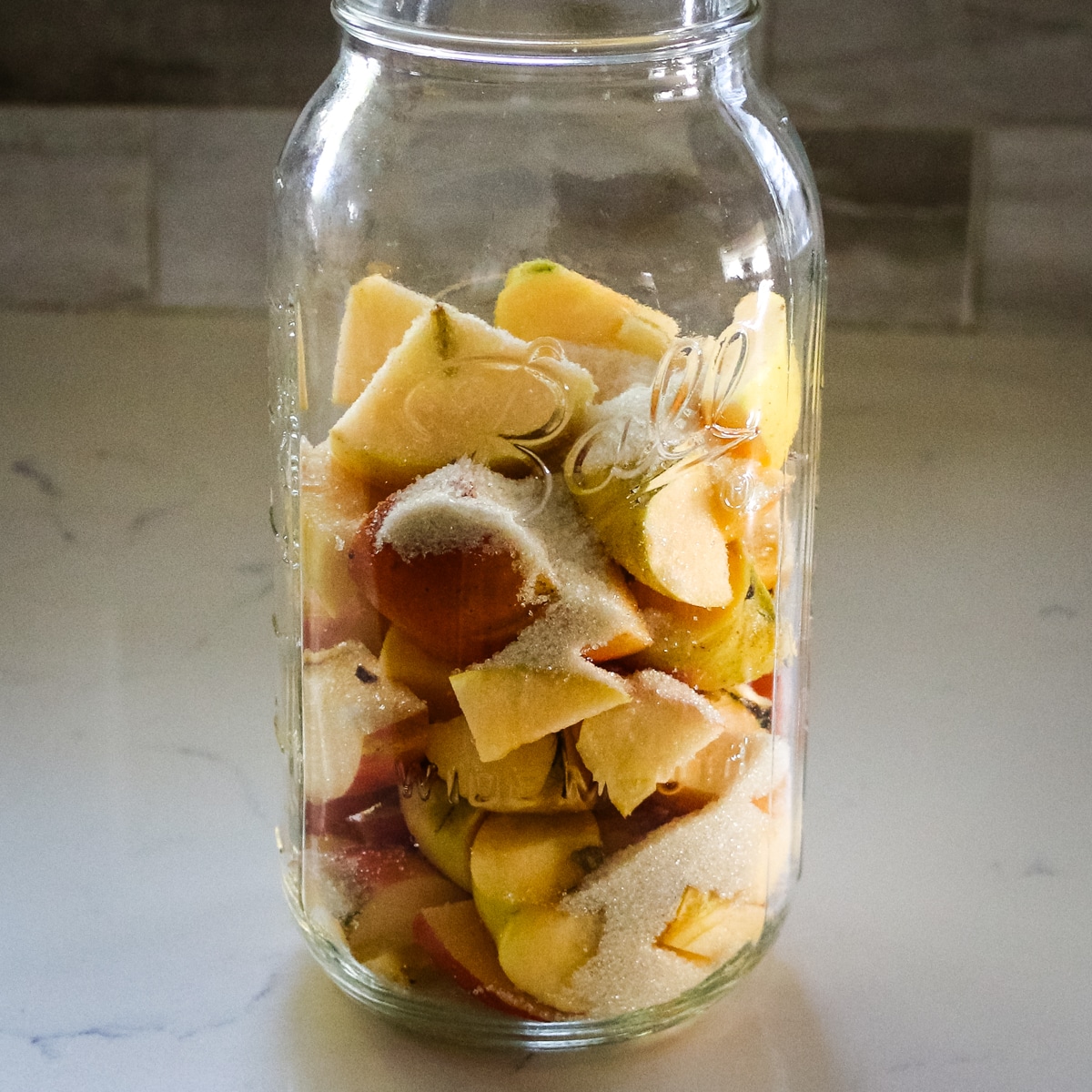 chopped apple scraps sprinkled with sugar inside a clear mason jar, ready for fermentation.