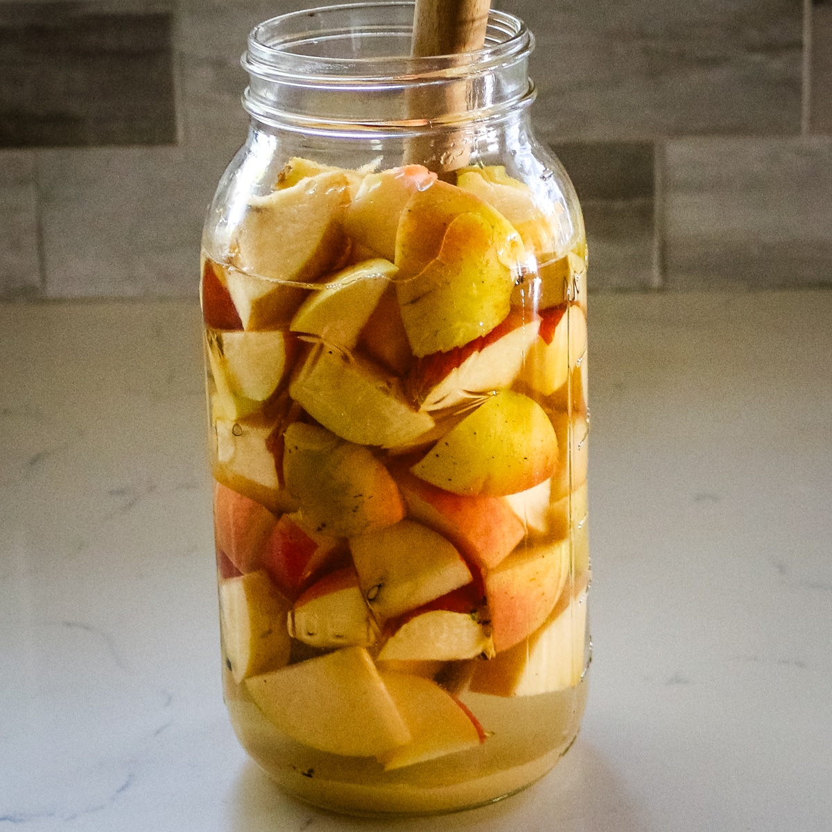 large glass jar filled with chopped apples and liquid for fermentation.