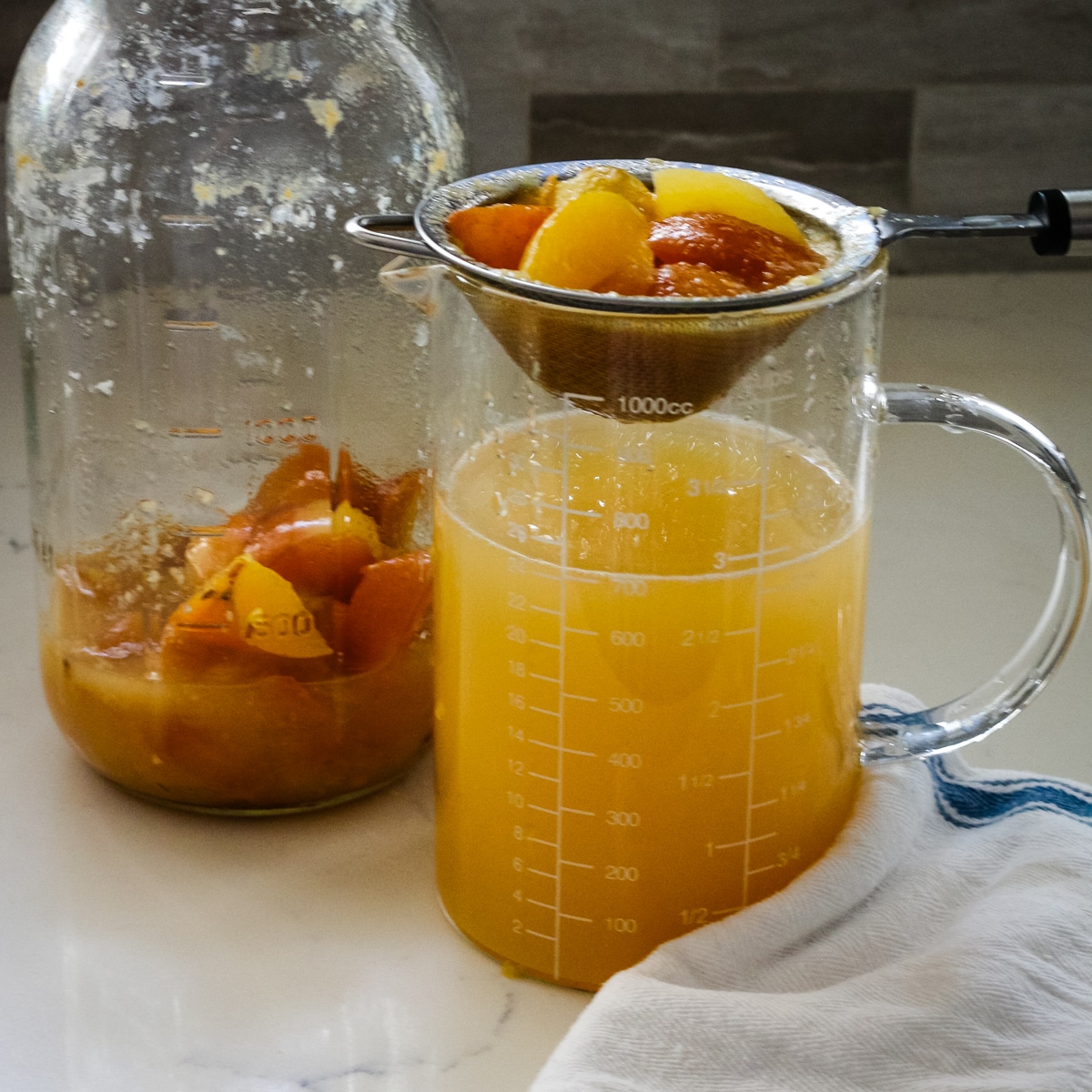 large glass jar and measuring cup showing the process of straining fermented apple solids from the liquid.