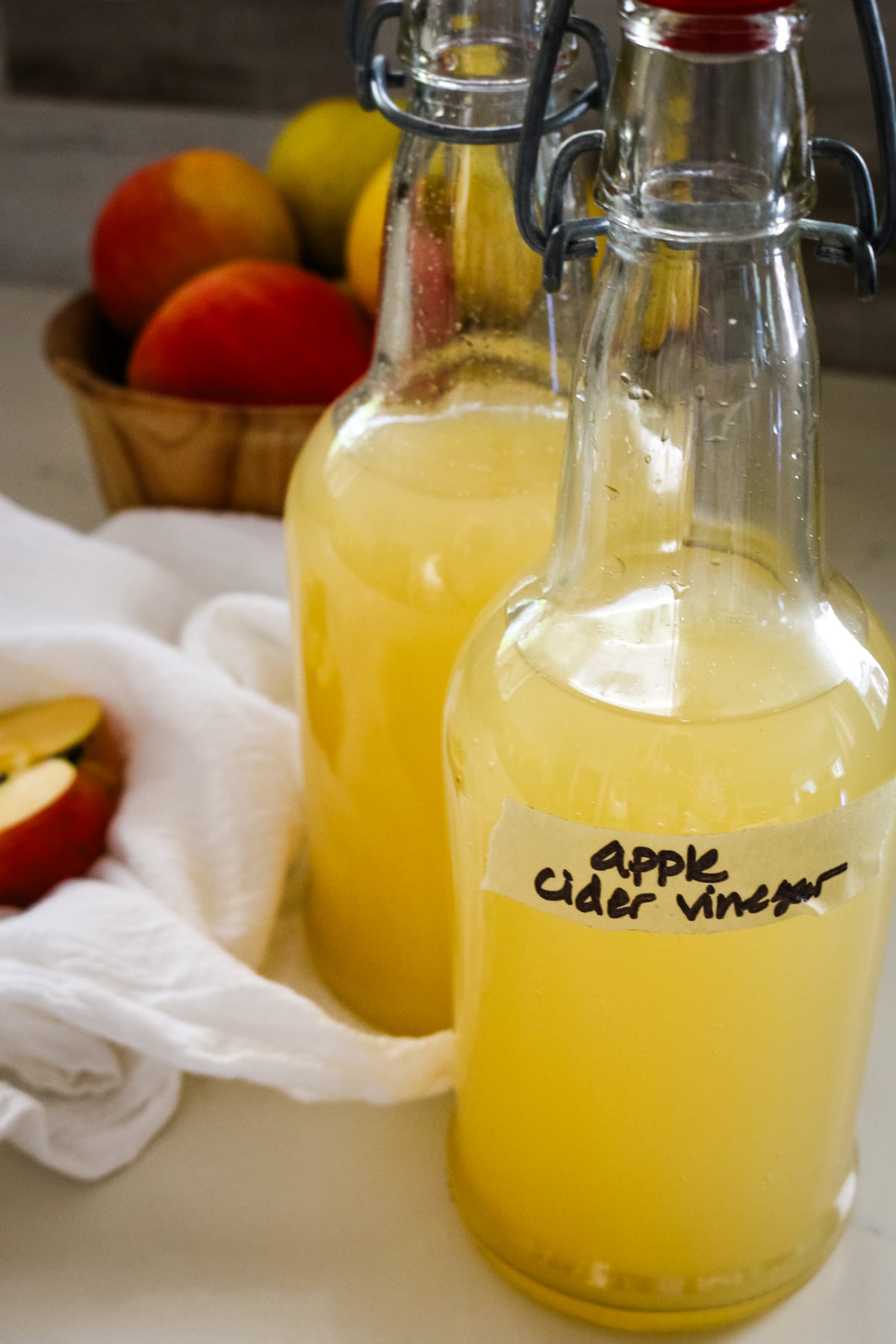 two swing-top bottles of homemade apple cider vinegar next to a bowl of fresh apples.