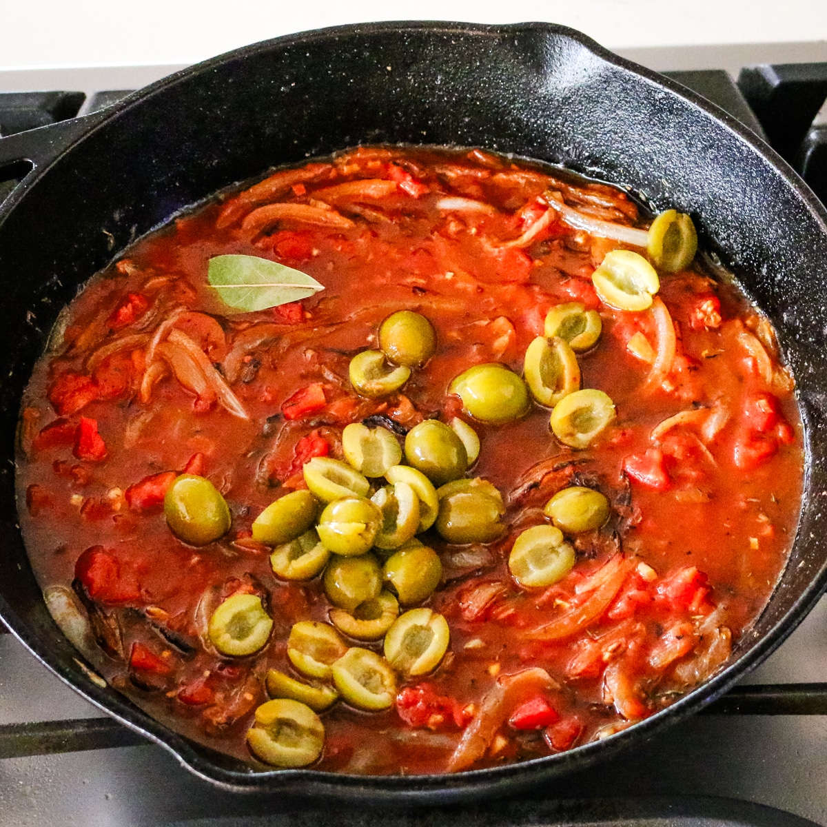 tomato sauce, peppers, and olives in a skillet.