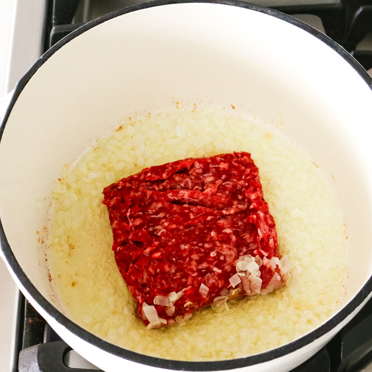 ground beef added to sautéed onions in a pot.
