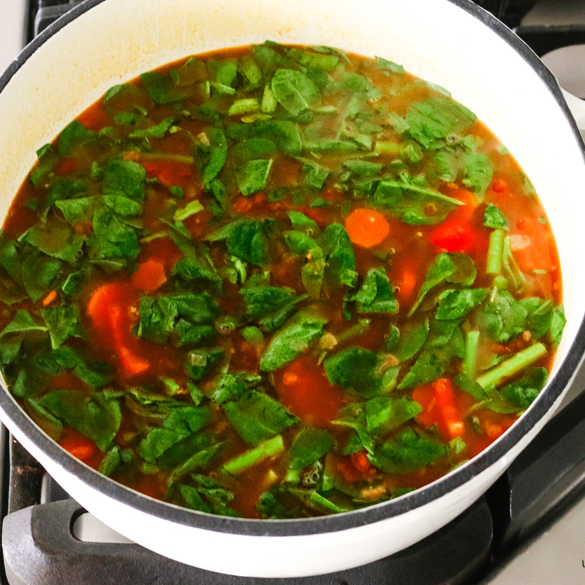 ground beef and vegetable soup with spinach simmering in a pot.