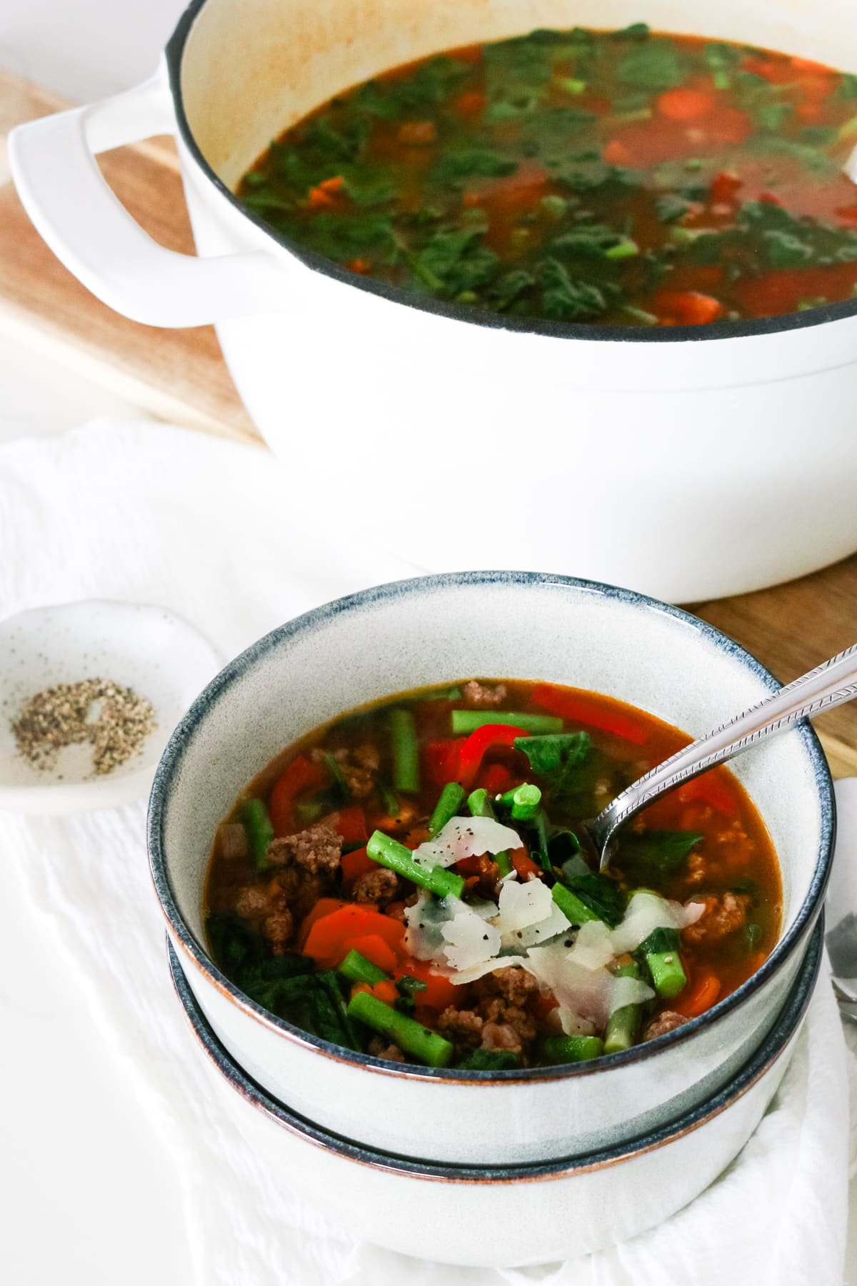ground beef and vegetable soup in a pot and served in a bowl.