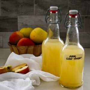 two swing-top bottles of homemade apple cider vinegar next to a bowl of fresh apples.