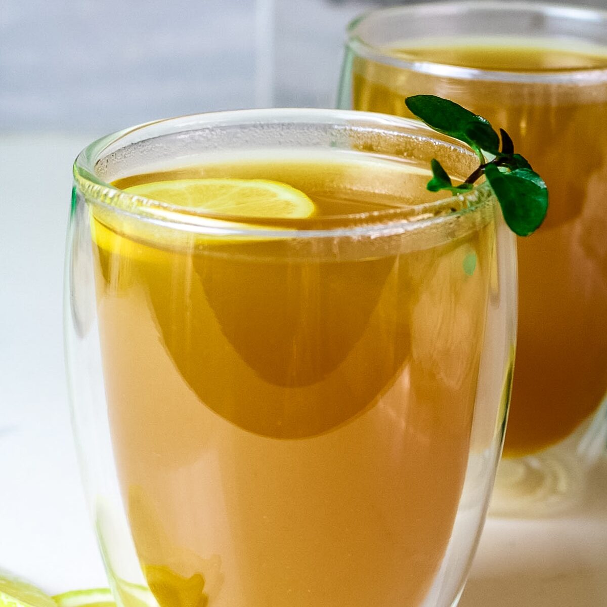 clear cups with honey citrus mint tea and lemon slices and edges and fresh mint as garnish.