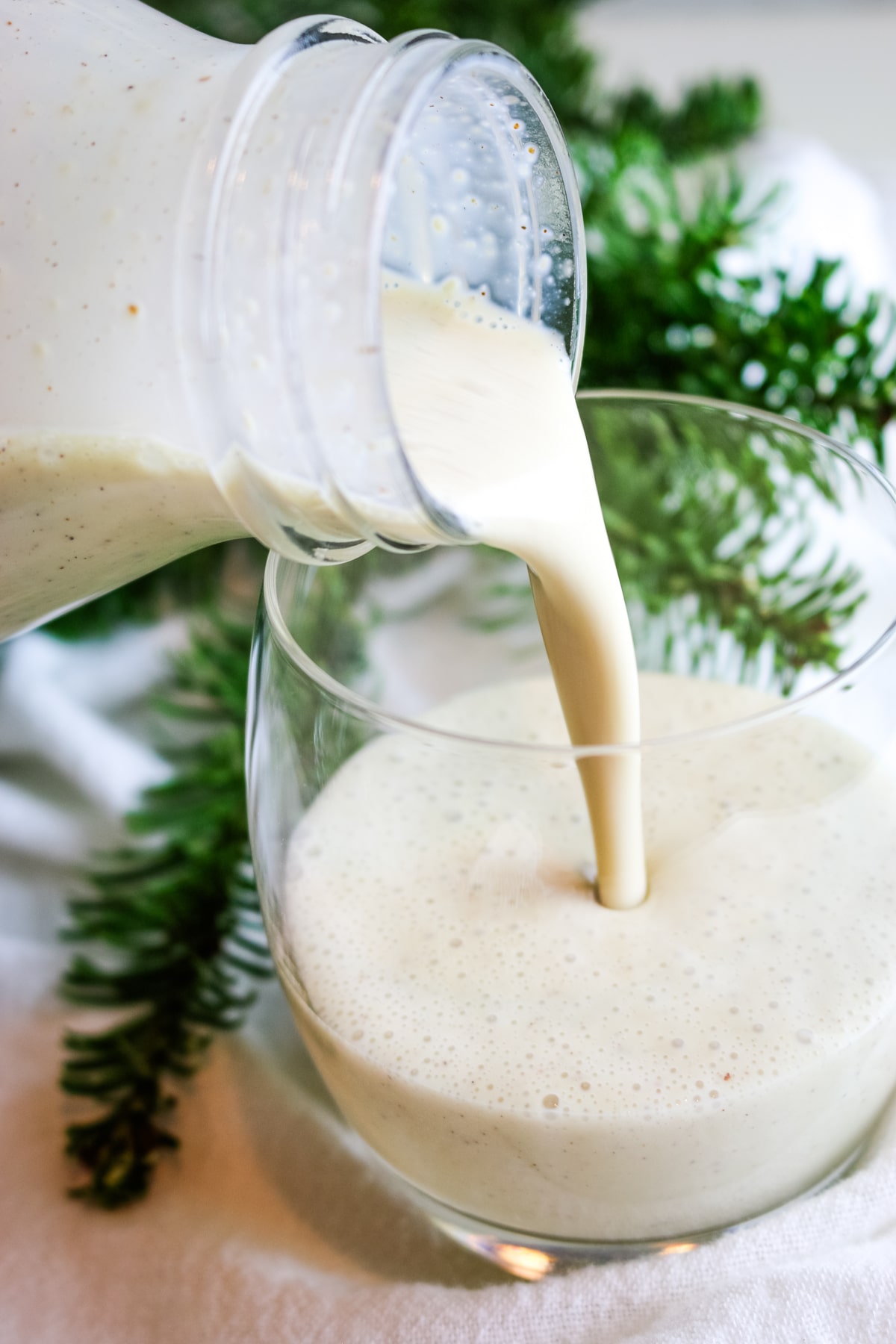 A thick, creamy drink is being poured from a clear bottle into a glass. The drink is pale and frothy.