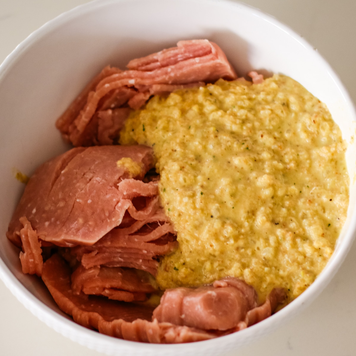 close-up of ground chicken slices and a yellow, wet bread binder in a white mixing bowl.