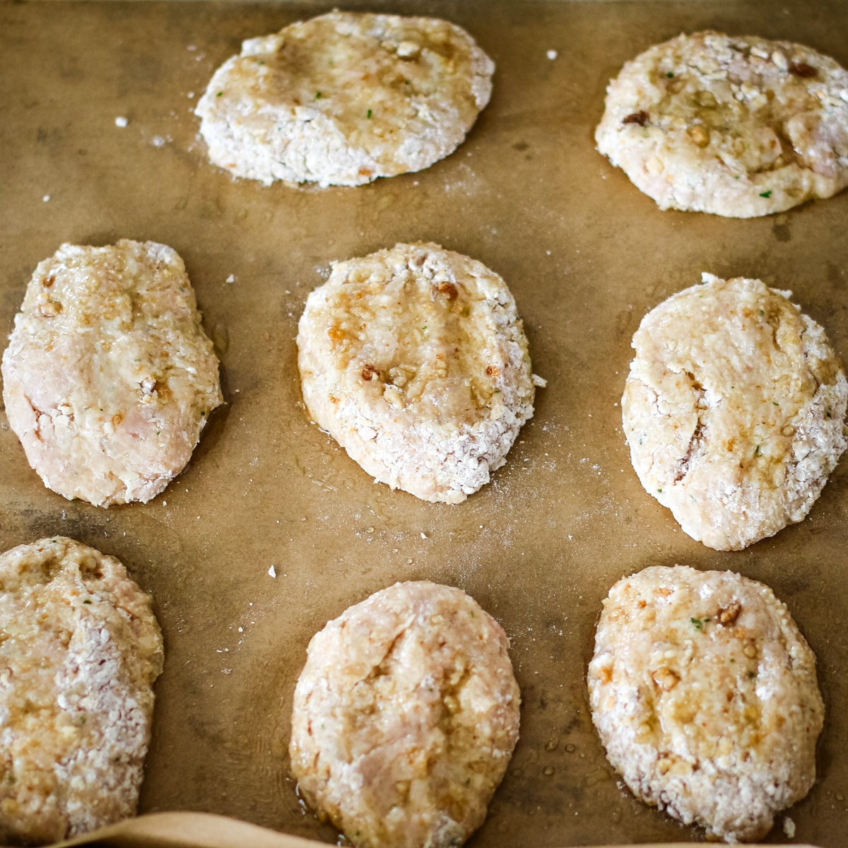 uncooked, flattened chicken kotleti resting on a sheet of brown parchment paper.