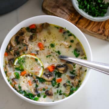 Turkey soup in a white bowl with a spoon and slice of lemon.