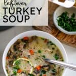 Turkey soup in a white bowl wtih a spoon and a slice of lemon, next to a cutting board and a pot full of turkey soup, with text above wit the title of the recipe.