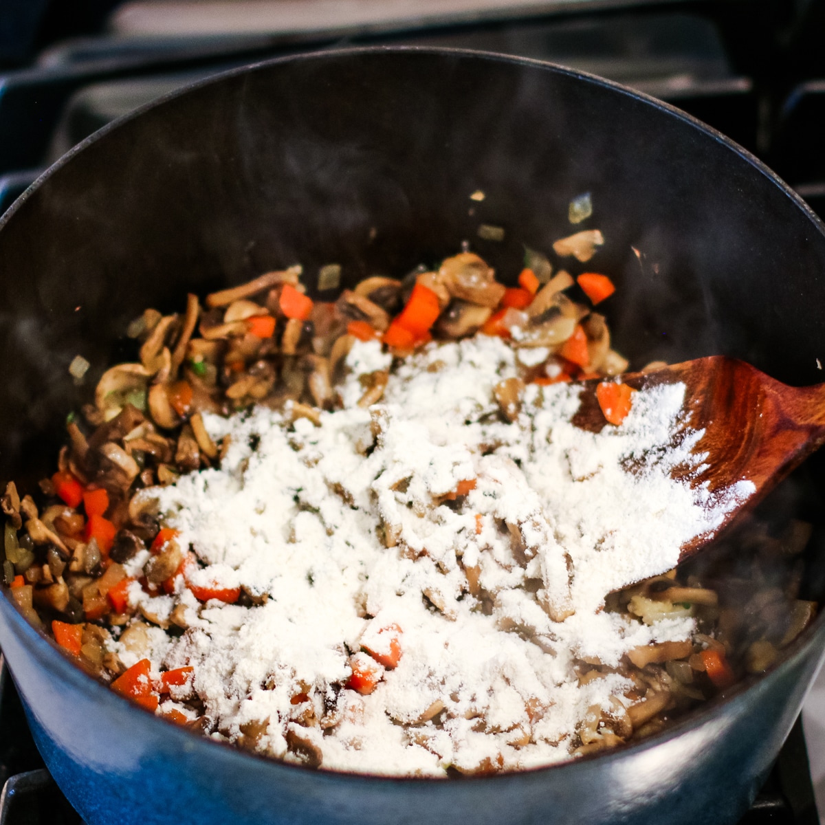 Diced onion, mushrroms, and carrots sauted in a pot, with flour sprinkled over.