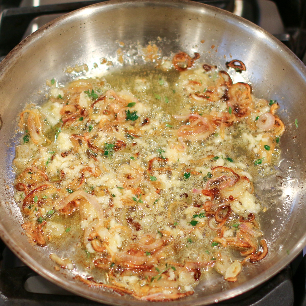 sautéed garlic and shallots sizzling in butter in a stainless steel pan.