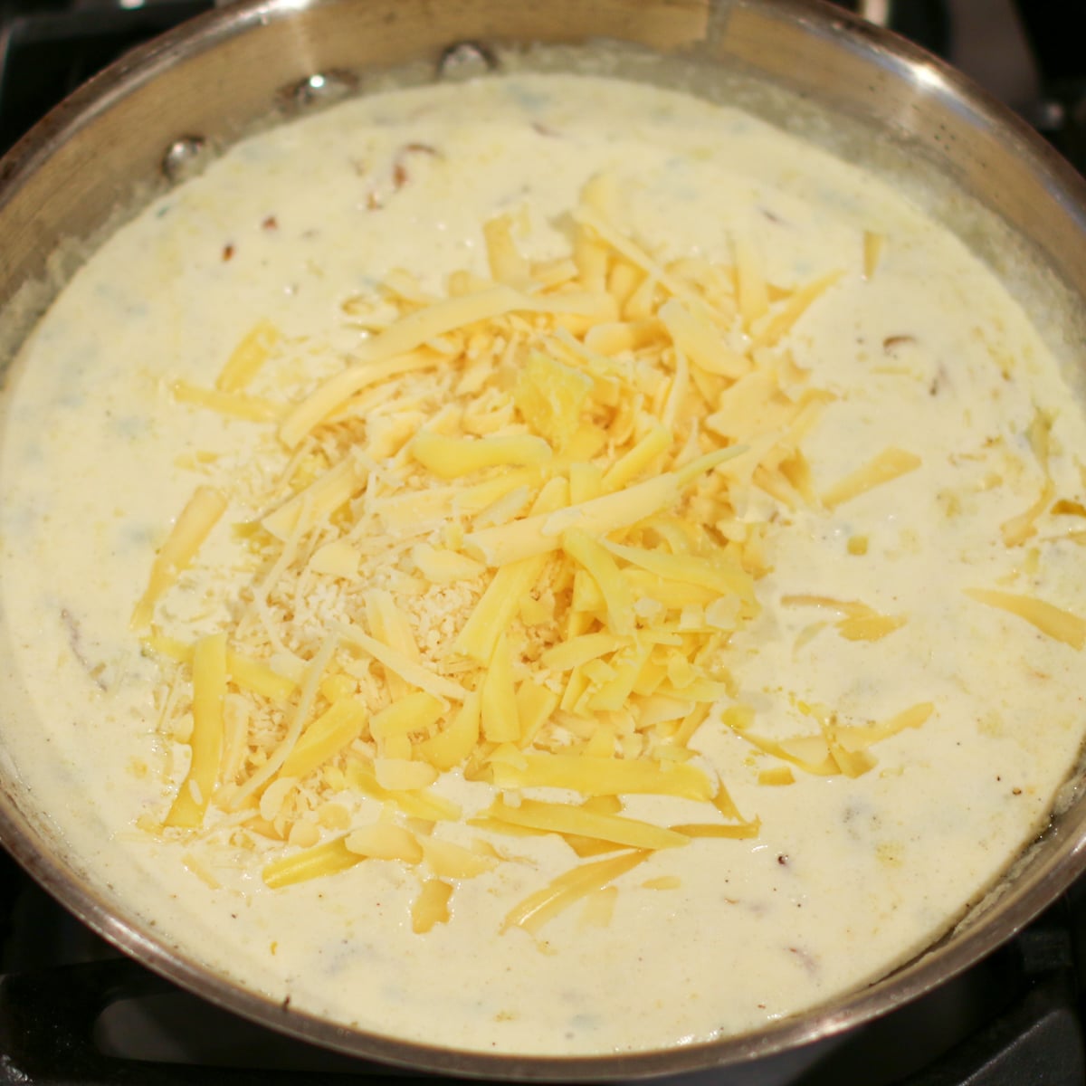 gruyère and parmesan cheeses being stirred into a pan, melting into a smooth, creamy sauce.