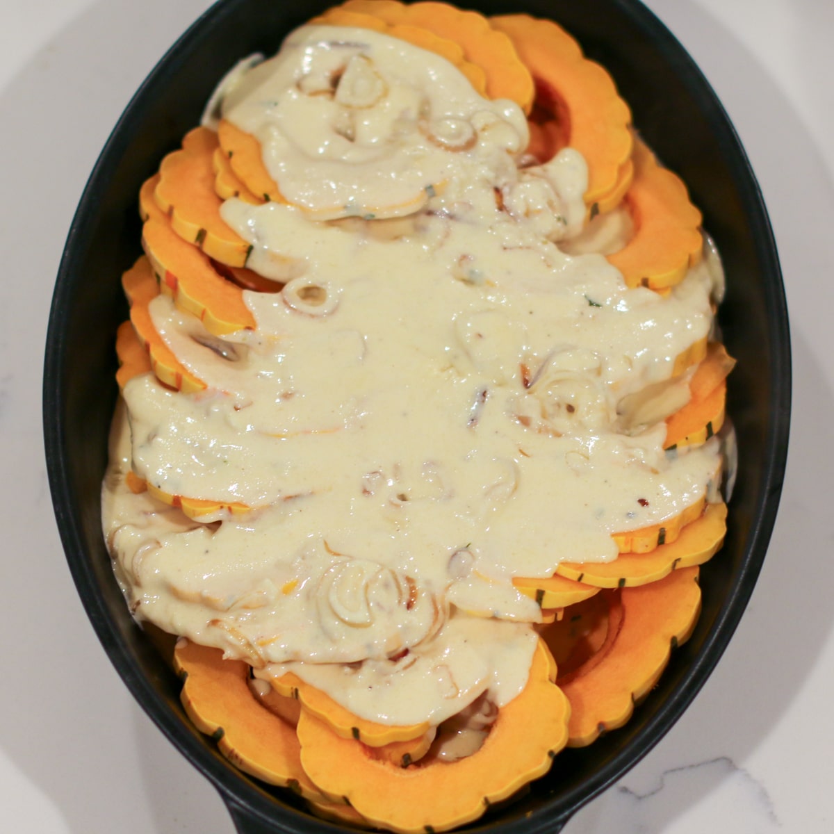 onion-cream sauce poured over delicata squash, spread evenly with a spoon to coat all slices.