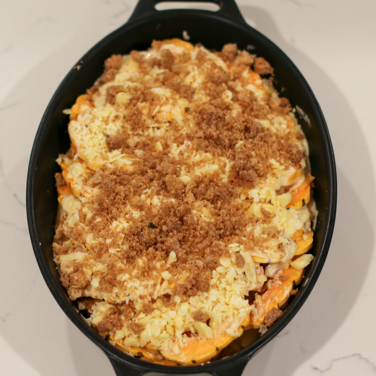 gruyère and parmesan cheese, along with breadcrumbs, sprinkled over squash in a baking dish.