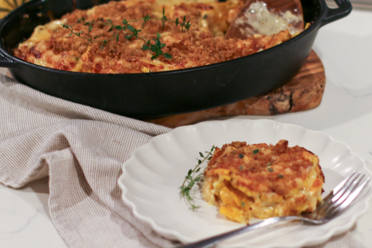 plated slice of Delicata Squash Au Gratin with a crispy breadcrumb topping, served beside the full gratin in a cast-iron skillet.