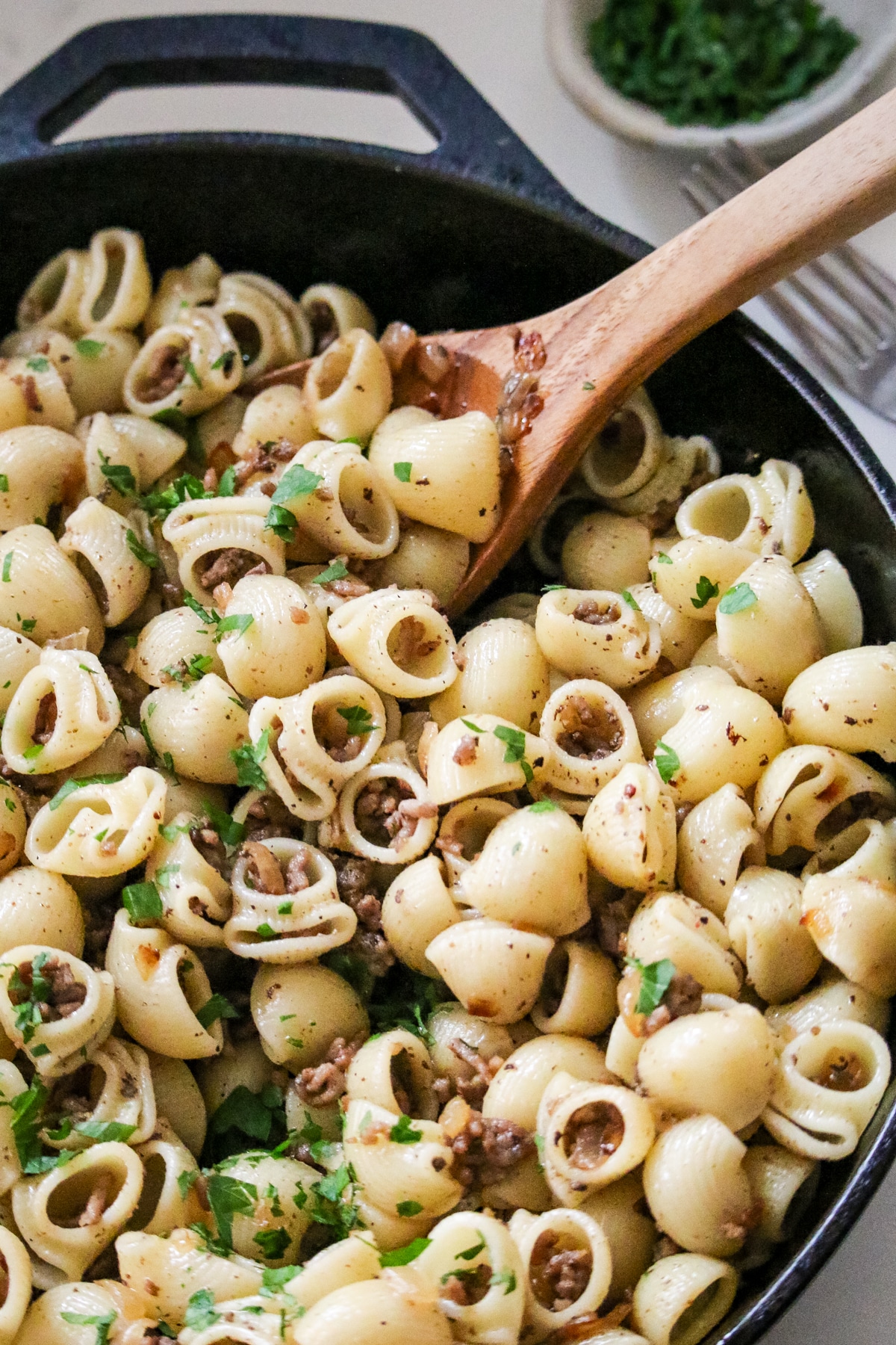 Ground beef tossed with shell pasta in skillet, lightly seasoned and finished with chopped parsley.