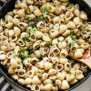 Ground beef tossed with shell pasta in a skillet, lightly seasoned and finished with chopped parsley.