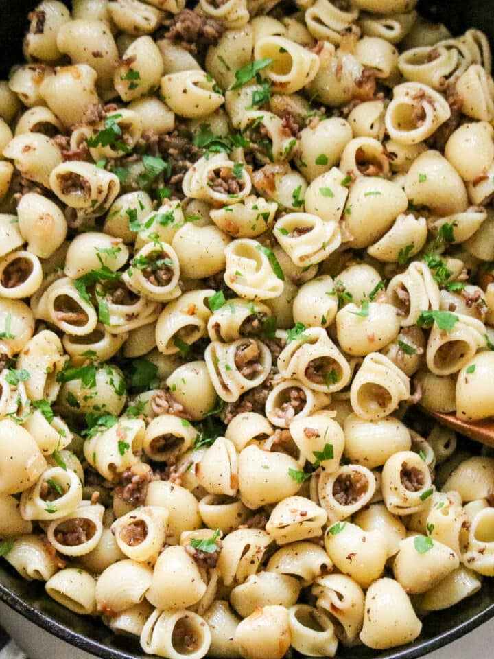 Ground beef tossed with shell pasta in a skillet, lightly seasoned and finished with chopped parsley.