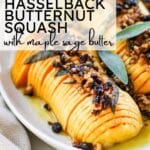 sliced hasselback butternut squash drizzled with melted butter and finished with a crunchy nut-and-dried-fruit topping, garnished with fresh sage on a white platter.