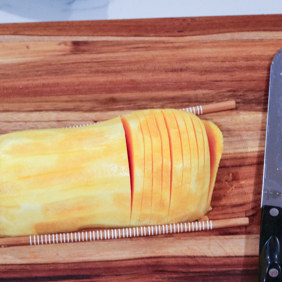 hasselback-cut butternut squash half on a wooden board, guided by chopsticks.