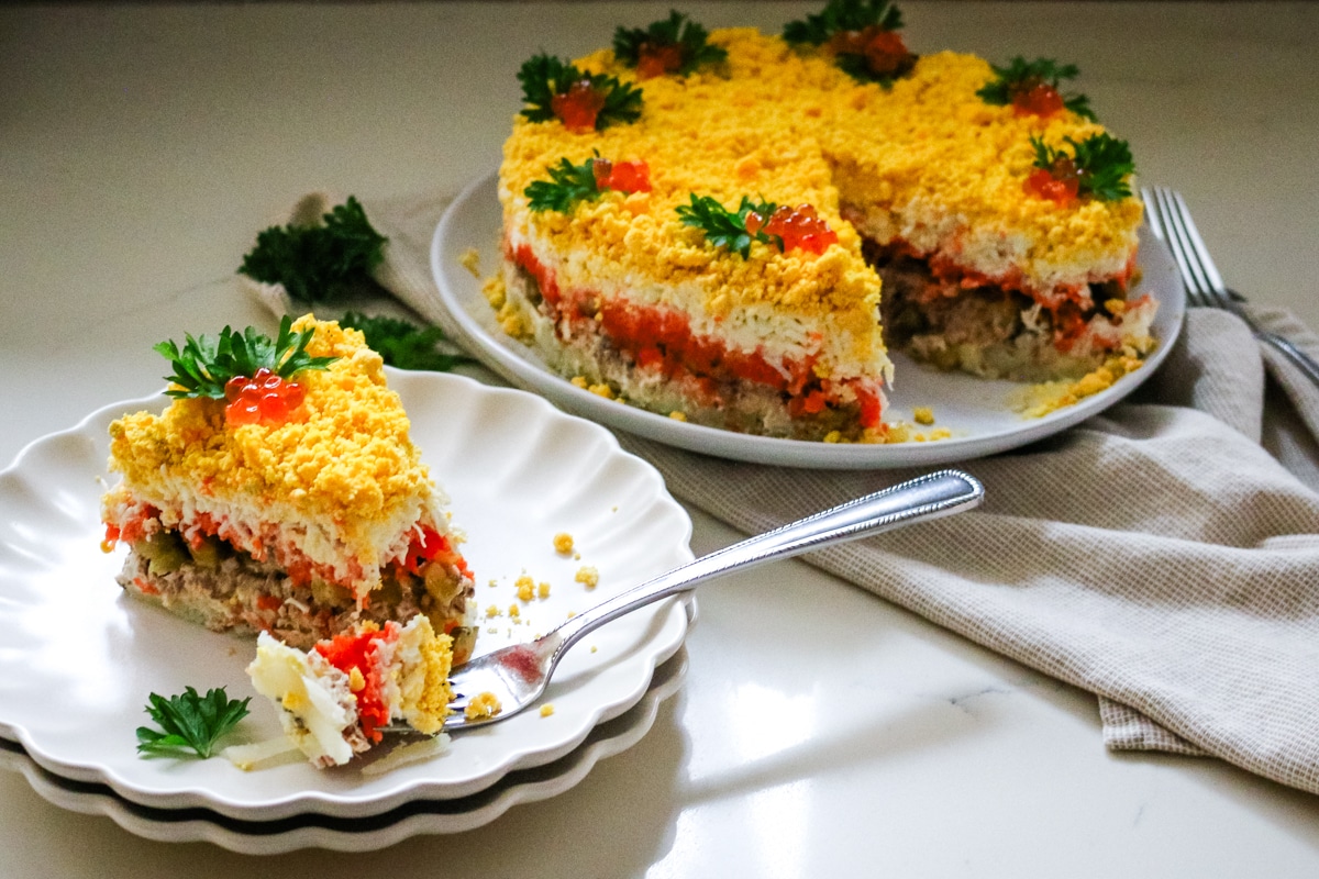 mimosa salad cut into with a wedge of the layered salad on a white plate.