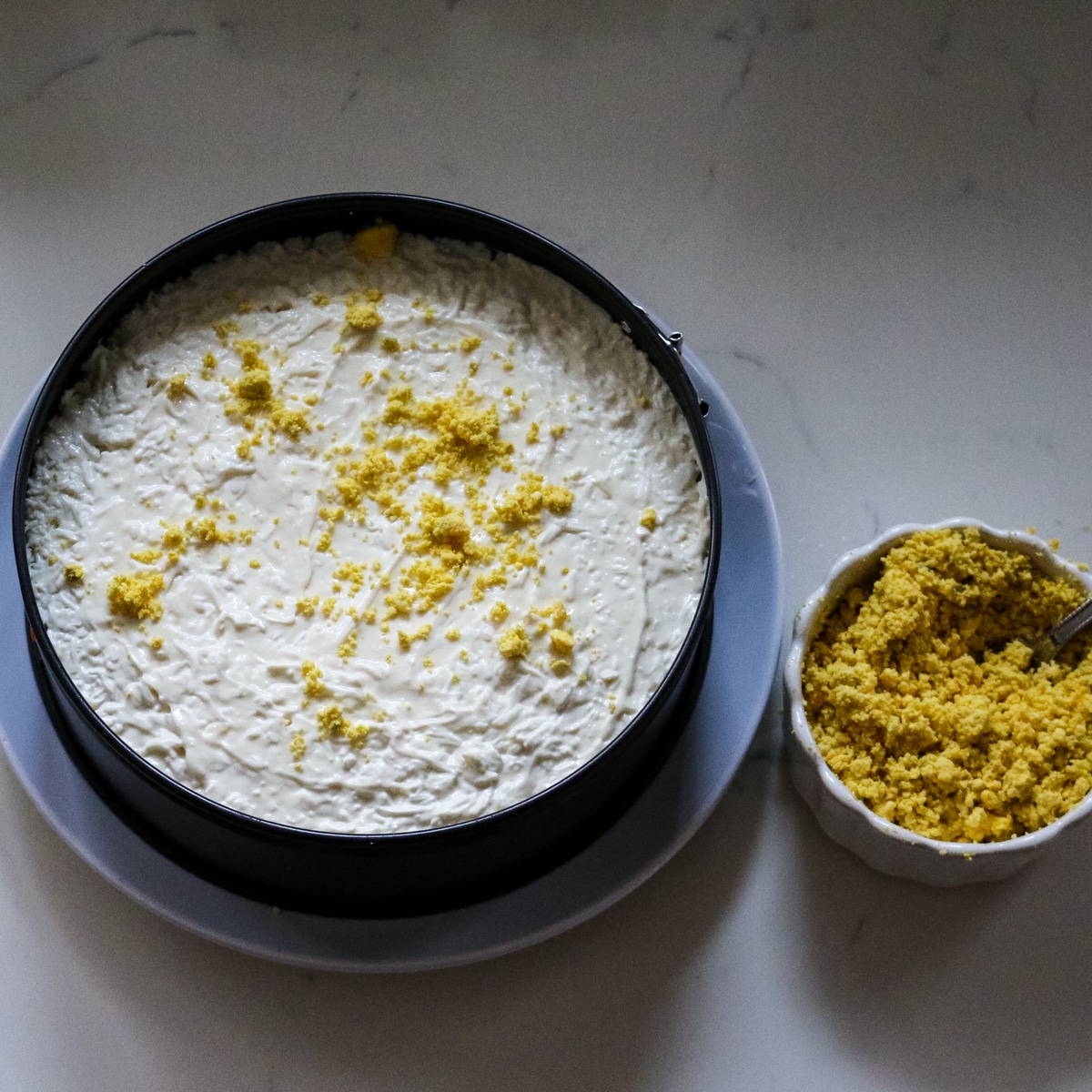 mimosa salad assembled in a springform pan, with a side bowl of crumbled egg yolks ready to be sprinkled on top.