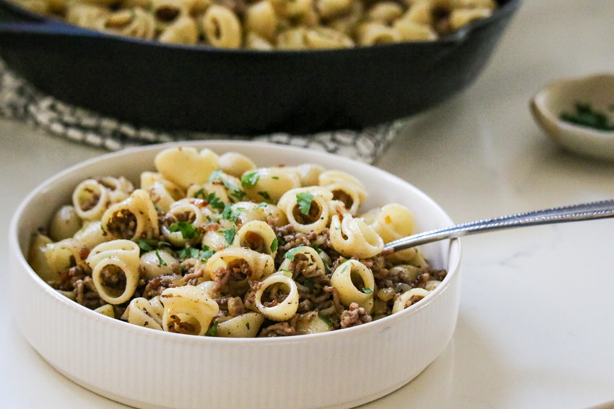 Ground beef tossed with shell pasta in bowl, lightly seasoned and finished with chopped parsley.