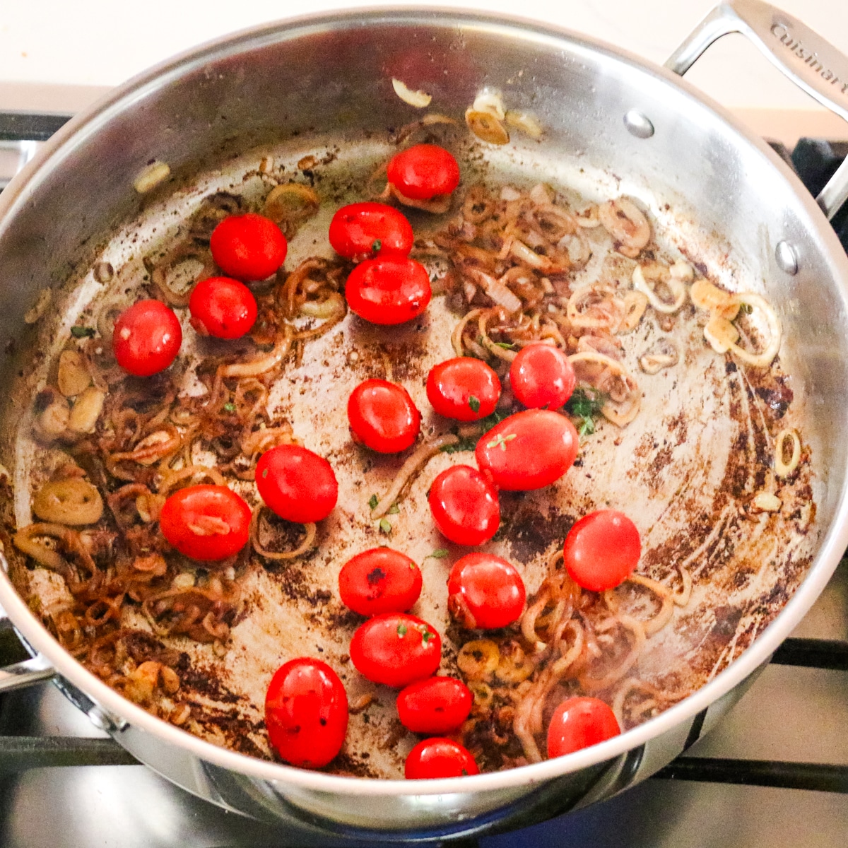 cherry tomatoes added to caramelized shallots in a stainless steel pan.