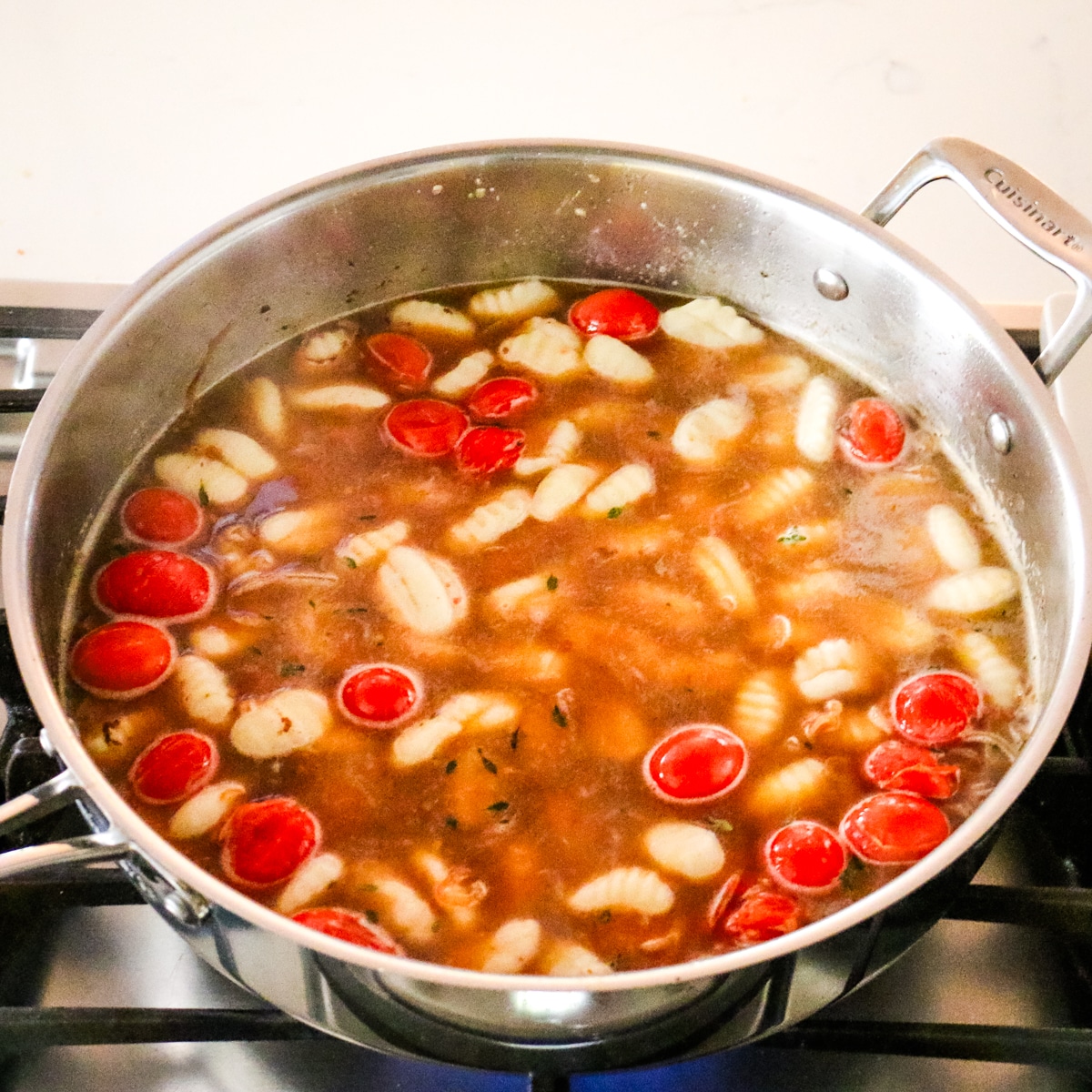 brothy gnocchi and sausage mixure with cherry tomatoes in a stainless steel pan.