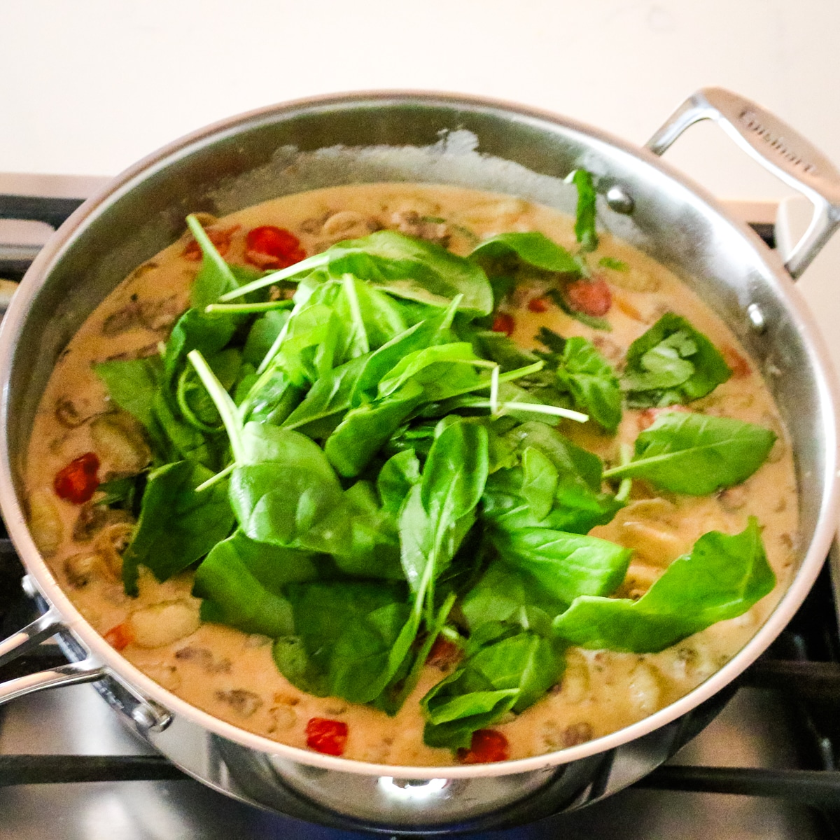 spinach added to creamy sausage and gnocchi in pan.