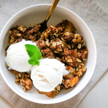 apple crisp in a bowl with vanilla ice cream and mint leaf as garnish.