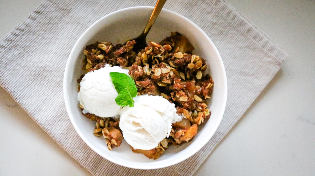 apple crisp in a bowl with vanilla ice cream and mint leaf as garnish.