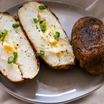 baked potatoes on a plate with butter and green onions.