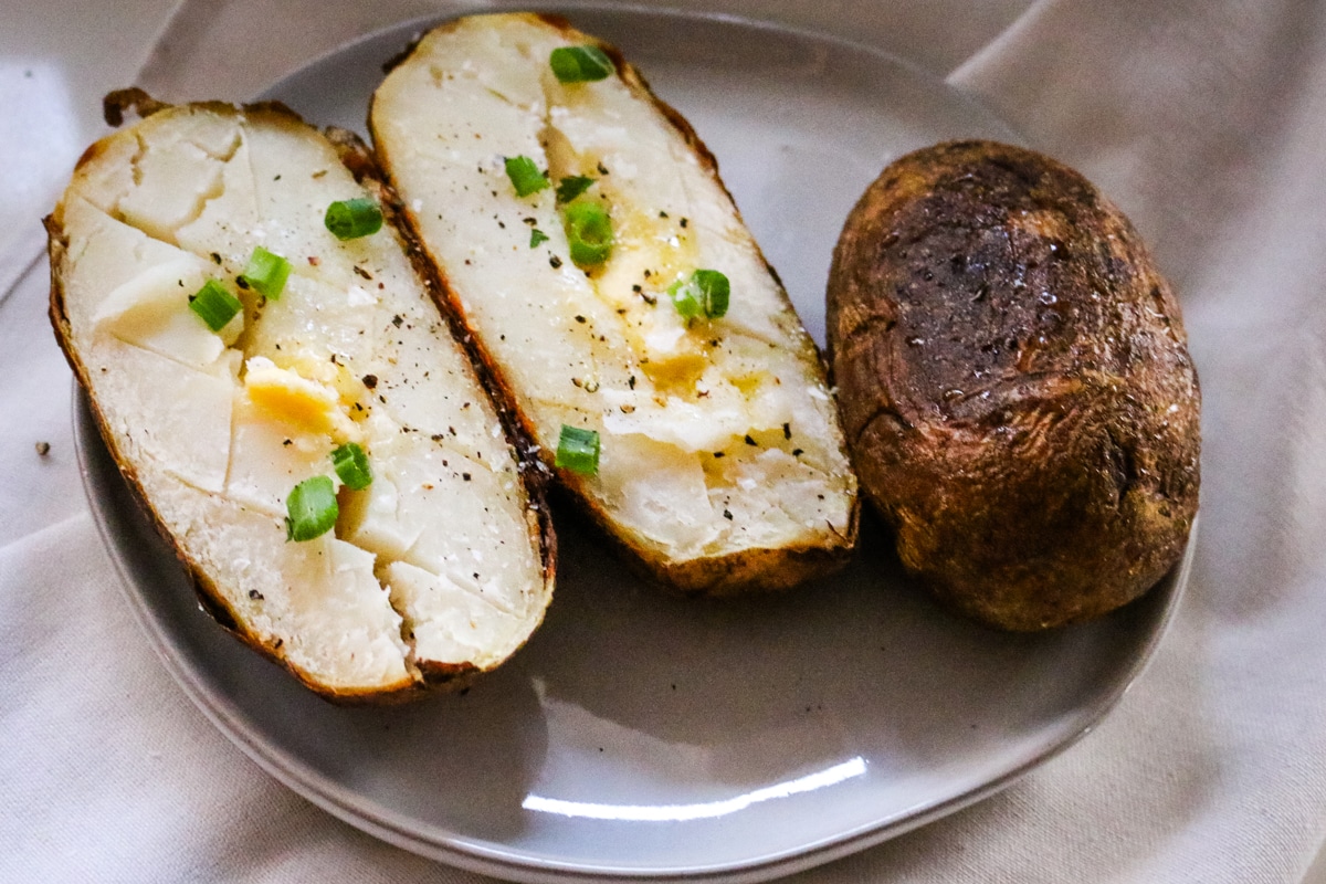 baked potatoes on a plate with butter and green onions.
