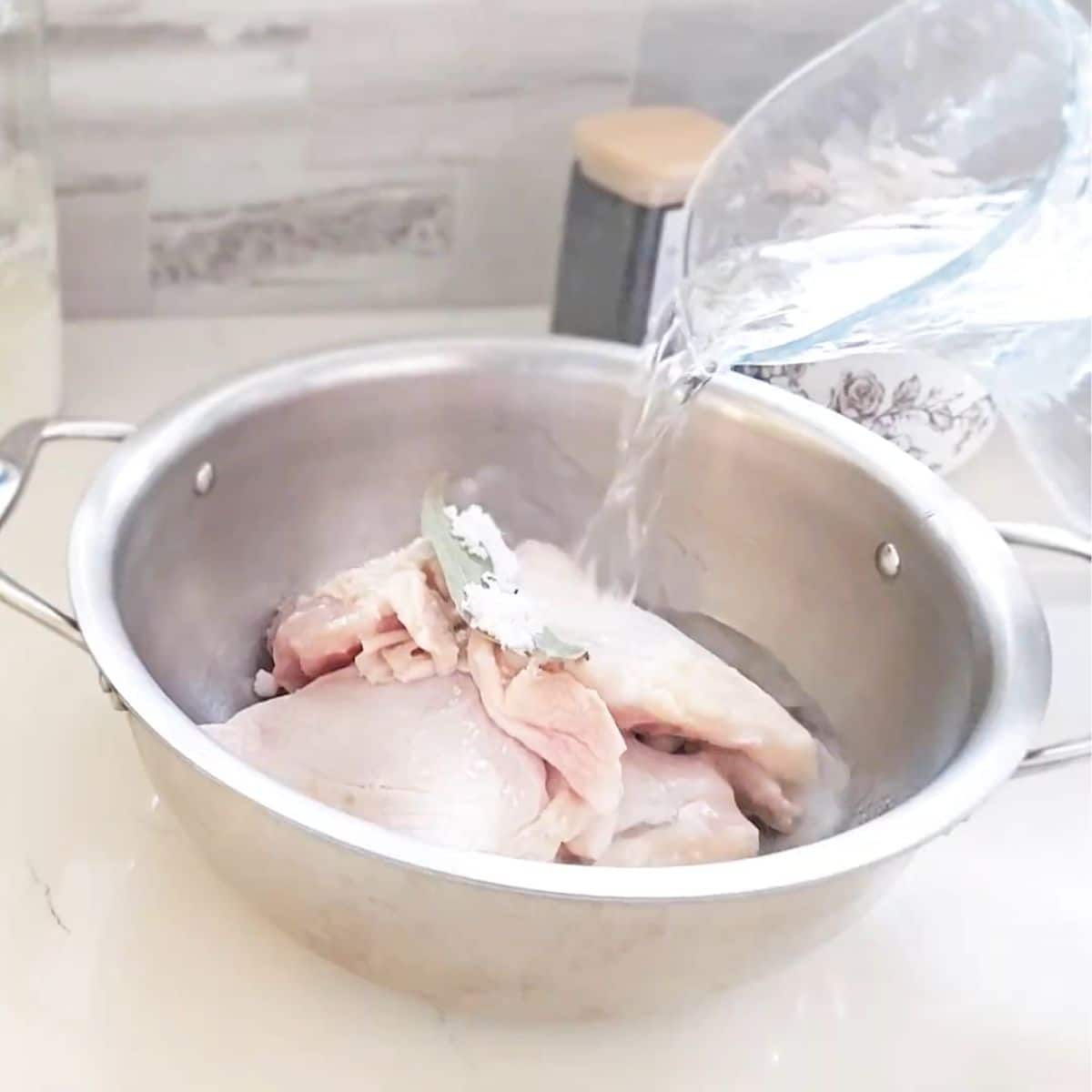 Chicken thighs, bay leaves, peppercorns, and salt simmered in water.