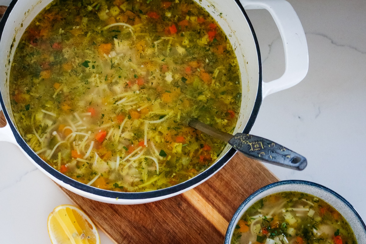 Romanian ciorbă soup served in a white pot and a white bowl.