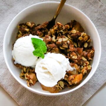 Apple crisp made with fresh-milled flour served in a bowl with a spoon and topped with vanilla ice cream.