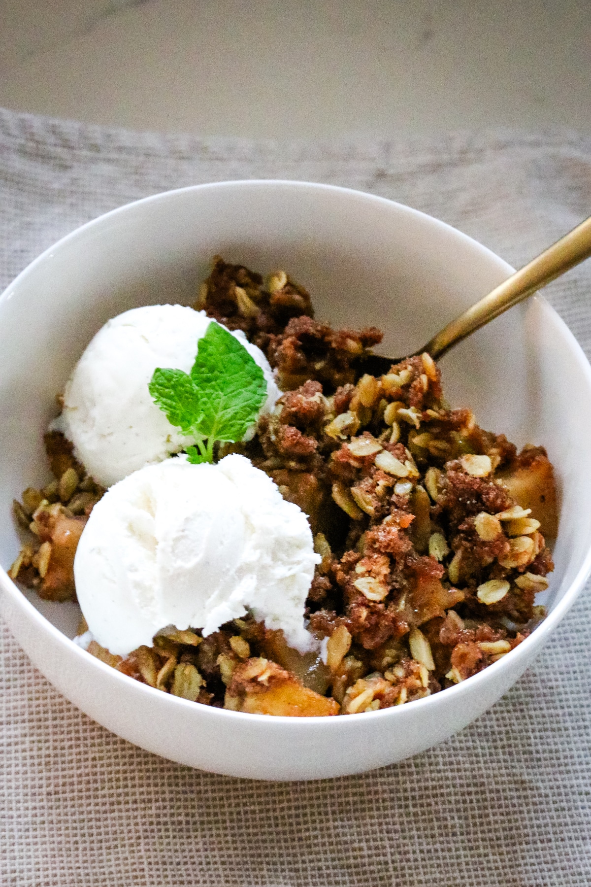 Apple crisp made with fresh-milled flour served in a bowl with a spoon and topped with vanilla ice cream.
