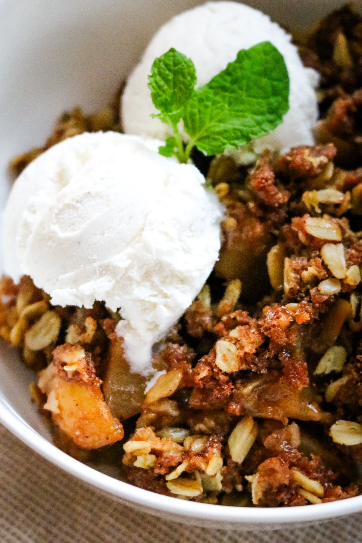 Apple crisp made with fresh-milled flour served in a bowl with a spoon and topped with vanilla ice cream.