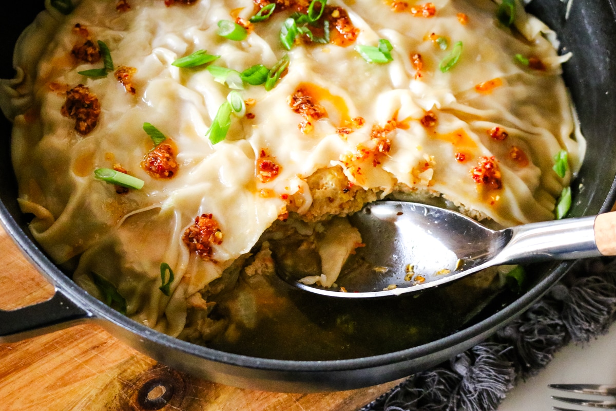 dumpling lasagna in a chistera saute pan with a spoon scooping.