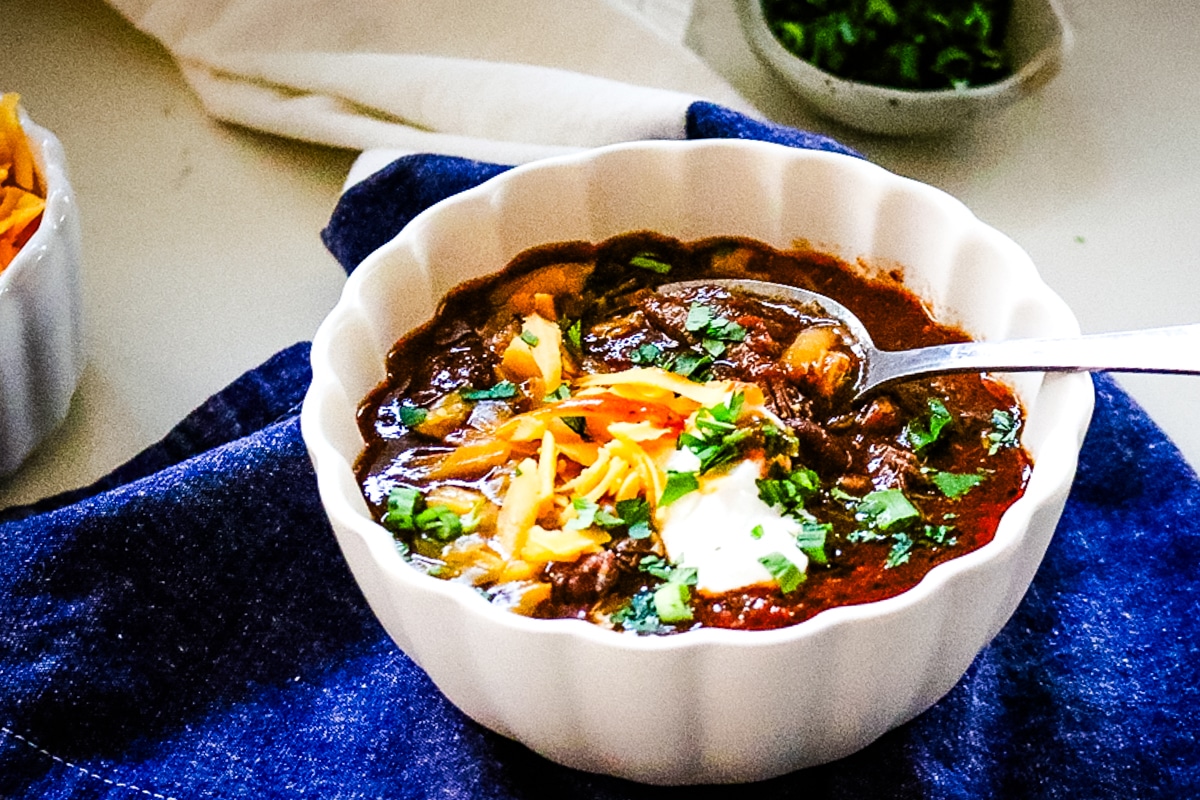 shredded beef chili in a white bowl with green onions in the back.