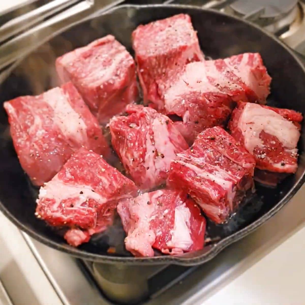 chunks of chuck roast in a cast iron skillet.