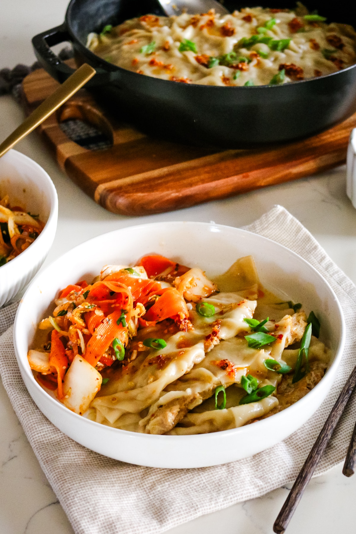 dumpling lasagna served in a bowl with chopsticks and dumpling lasagna in a chistera saute pan in the background.