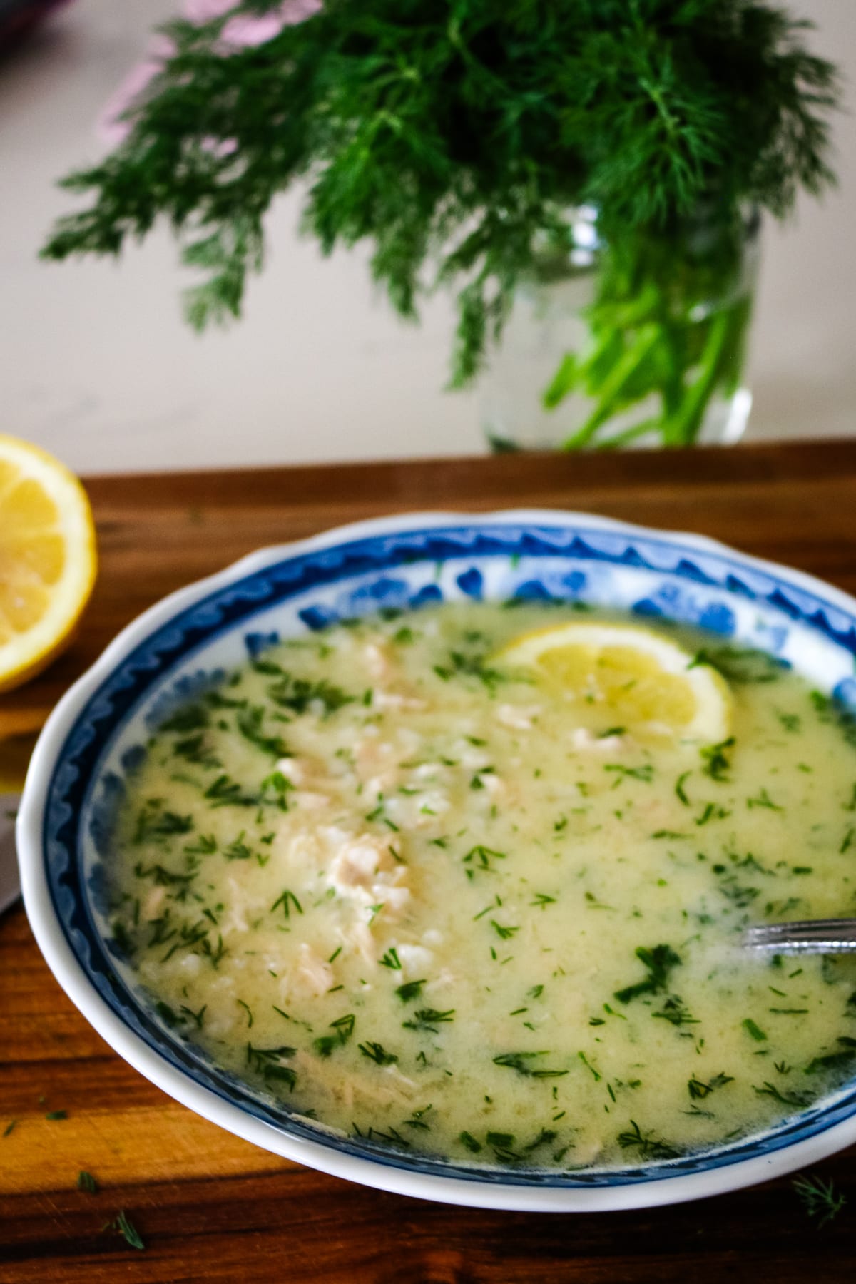 Avgolemono soup with lemon and shredded chicken, served with a spoon.