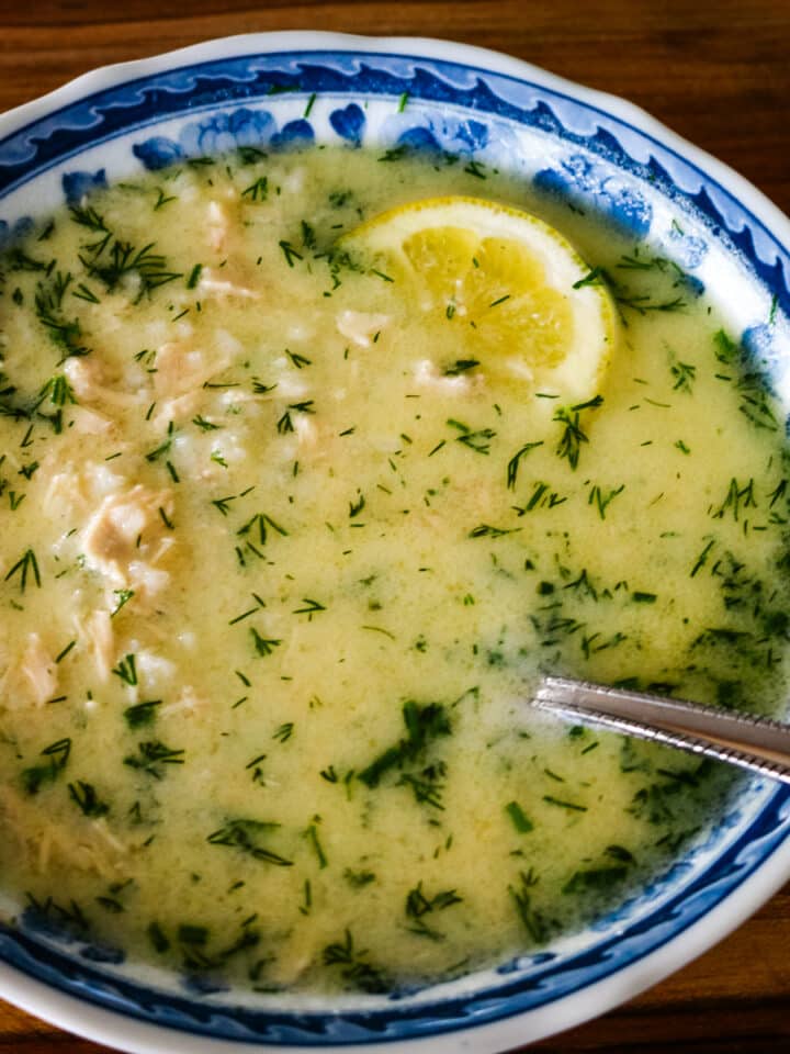 Avgolemono soup with lemon and shredded chicken, served with a spoon.