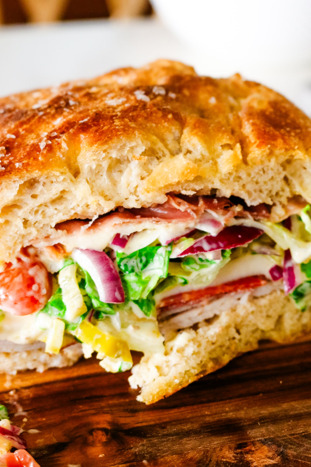grinder sandwich on a cutting board with red onions and lettuce.